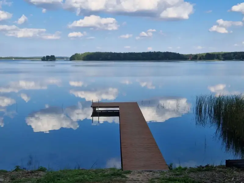 Spokojne jezioro Wągrowiec z drewnianym pomostem odbijającym chmury na błękitnym niebie.
